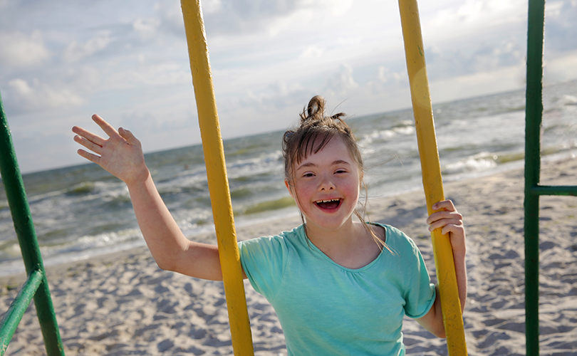 Ein Mädchen schaukelt am Strand und winkt in die Kamera