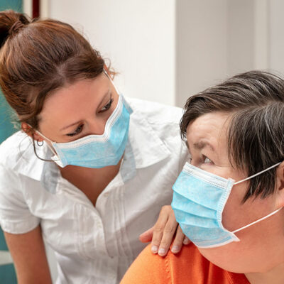 Eine Betreuerin spricht mit einer Klientin. Beide tragen Masken zum Schutz vor Corona.