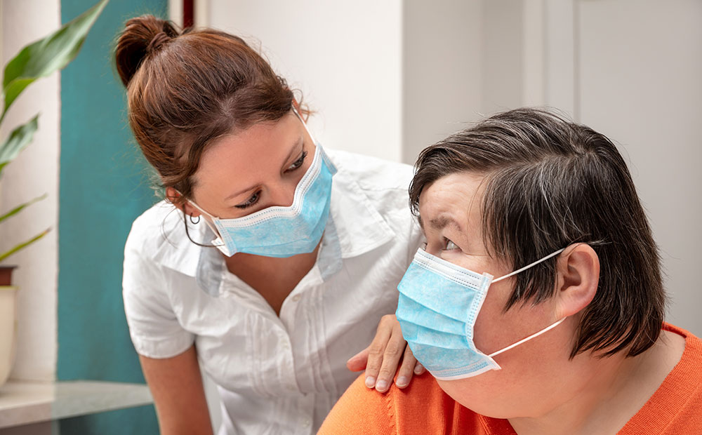 Eine Betreuerin spricht mit einer Klientin. Beide tragen Masken zum Schutz vor Corona.