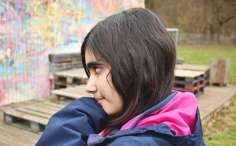 Ein Mädchen steht vor eine Graffiti-Wand.