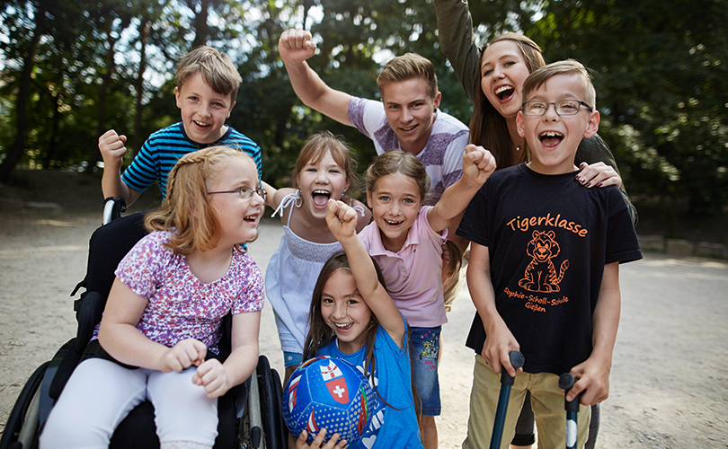 Eine Gruppe Kinder und Betreuer steht zusammen, hebt freudig die Arme in die Luft und freut sich. Es sieht aus als hätten Sie ein Ballspiel gewonnen.