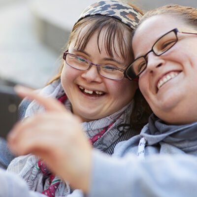 Zwei Frauen lachen und machen mit dem Handy ein Selfie von sich.