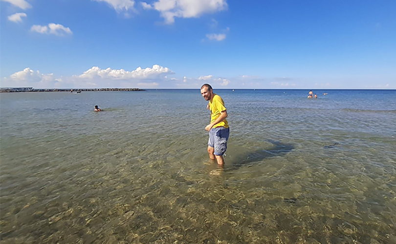 Ein Mann steht mit den Füßen im Meerwasser am Strand.