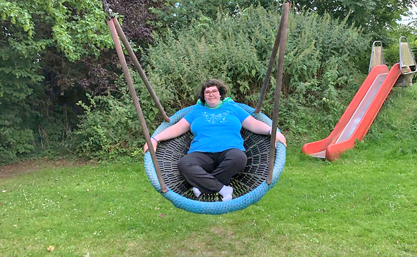 Eine Frau schaukelt. Im Hintergrund sieht man eine Rutsche.