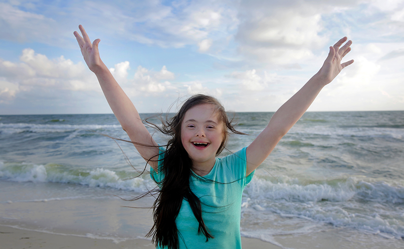 Ein Mädchen steht am Strand und hält beide Arme in die Luft. Das Bild sieht nach Freiheit aus.