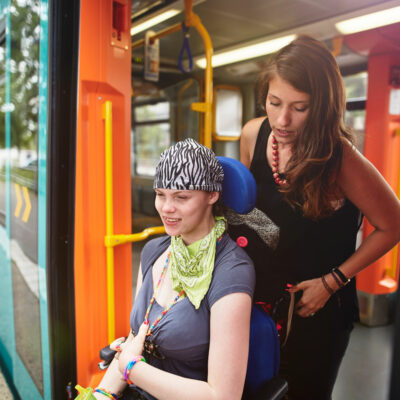 Eine Betreuerin und eine junge Frau im Rollstuhl steigen aus dem Zug aus.