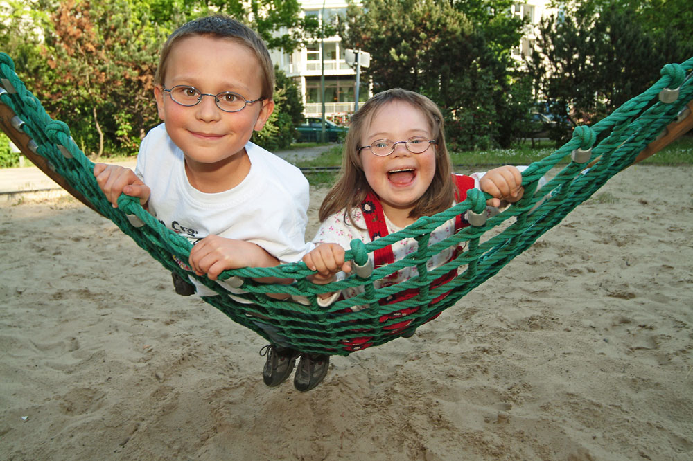 Zwei Kinder liegen auf einer Schaukel und bewegen sich damit Richtung Kamera.