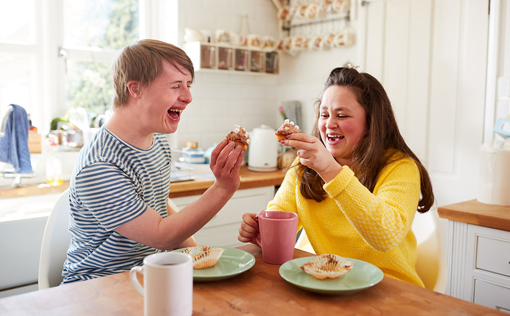 Ein Paar mit Trisomie 21 isst zuhause Kaffee und Kuchen. 
