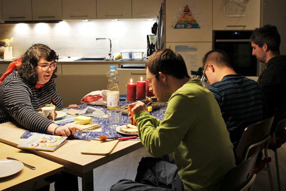 Mitbewohner und eine Mitbewohnerin einer Mitleben Wohngemeinschaft sitzen gemeinsam beim Abendessen an einem Tisch.
